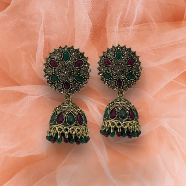 Antique gold jhumka earrings with red and green stones on white background