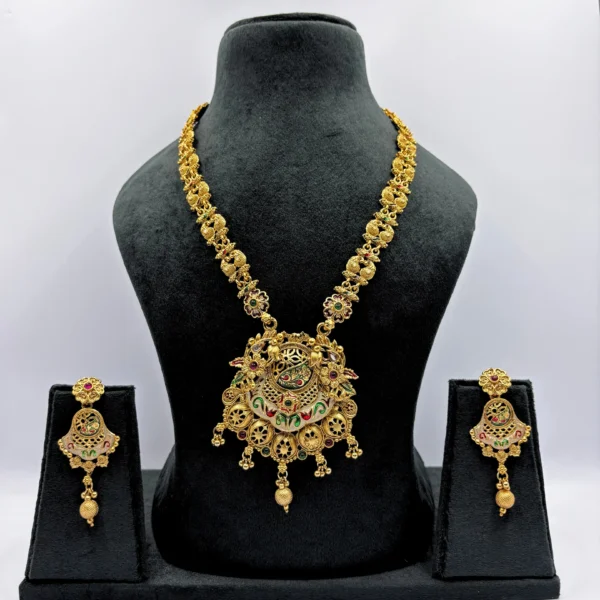 Antique gold-plated temple jewelry set with peacock pendant, meenakari detailing, and matching earrings displayed on a black bust stand against white background